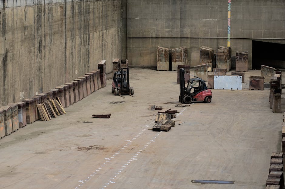 Two forklifts in a large industrial warehouse setting with stored machinery.